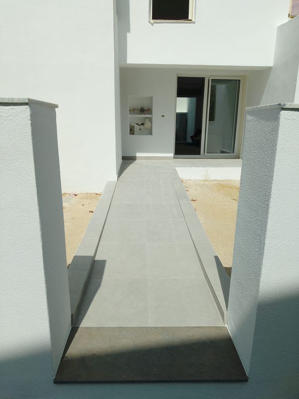 Rampa de entrada em pavimento cerâmico, entre muros rebocados e pintados